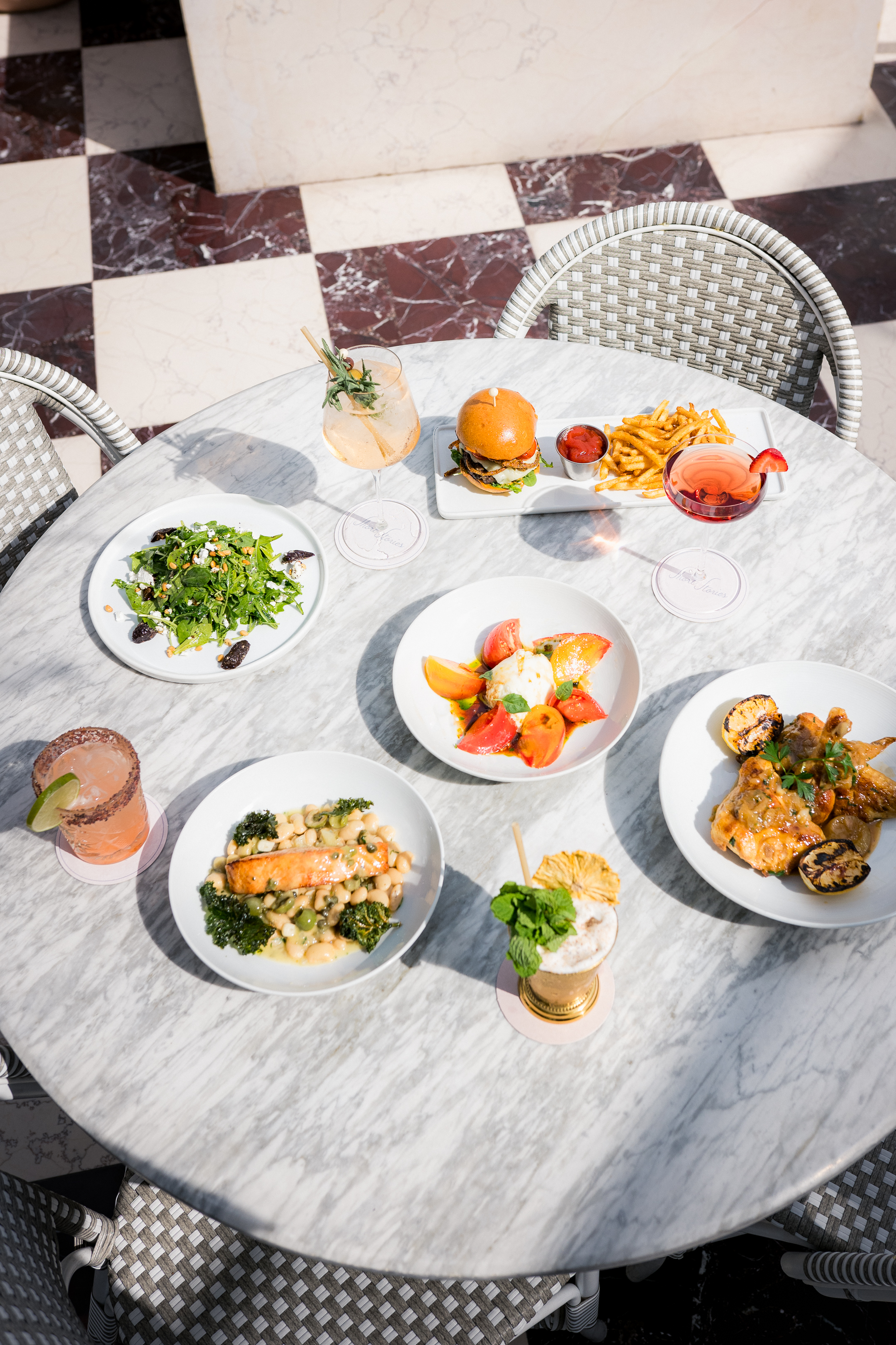 A round marble table with various dishes and drinks on it, surrounded by wicker chairs.