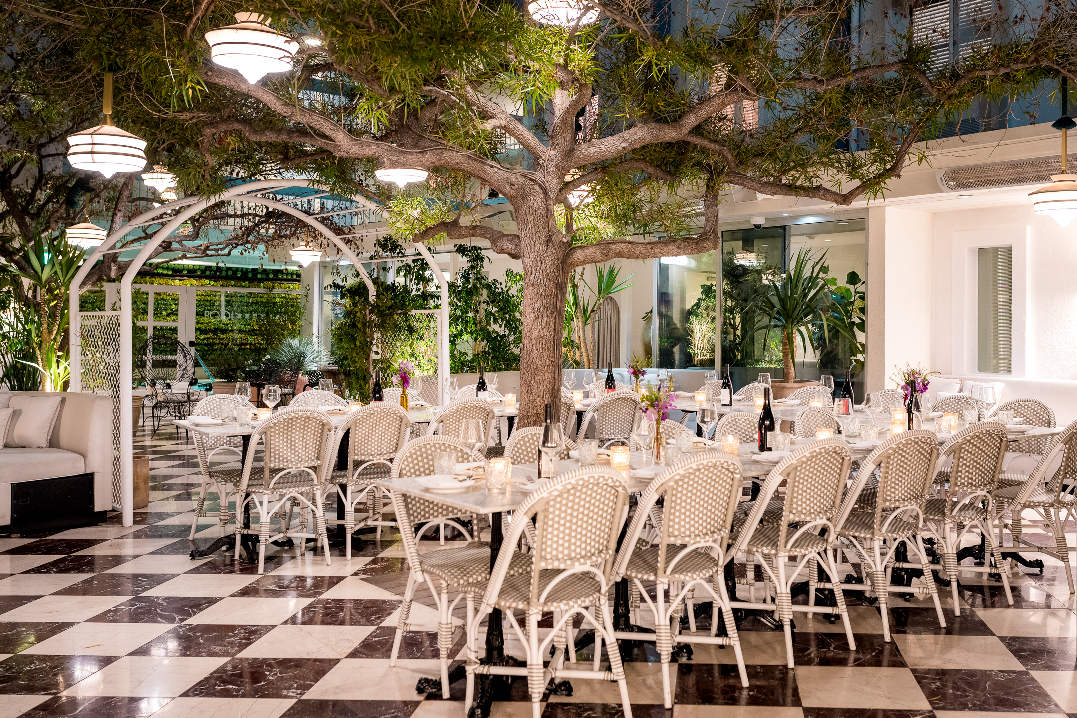 A dining area with white tables and chairs, a tree, and an archway.