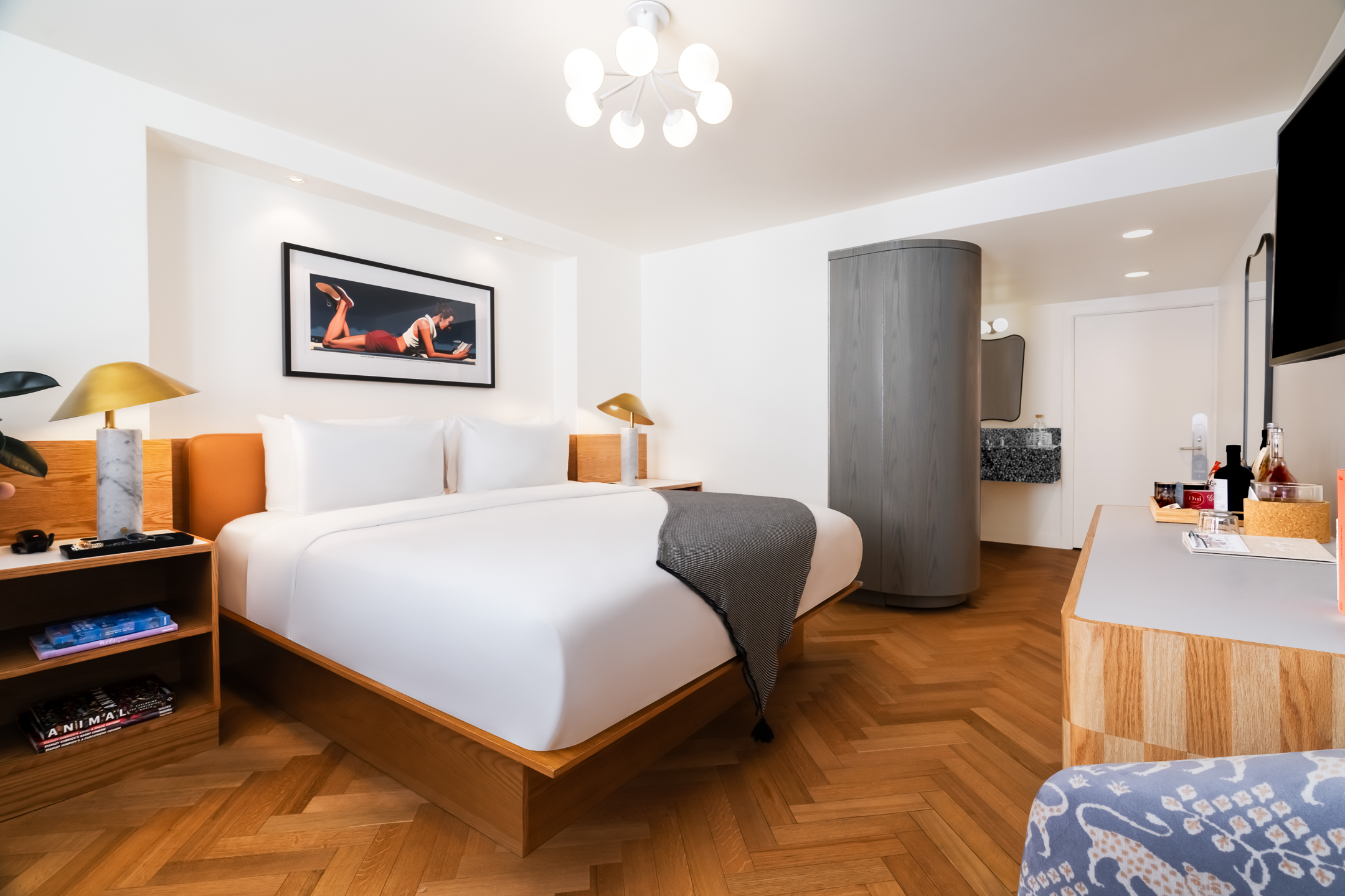 A hotel room with a large bed, two nightstands with lamps, a TV on the wall, and a desk.