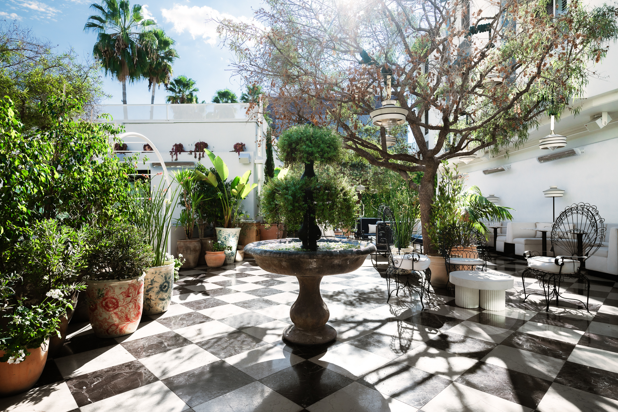 A serene outdoor courtyard with a fountain, potted plants, and seating areas.
