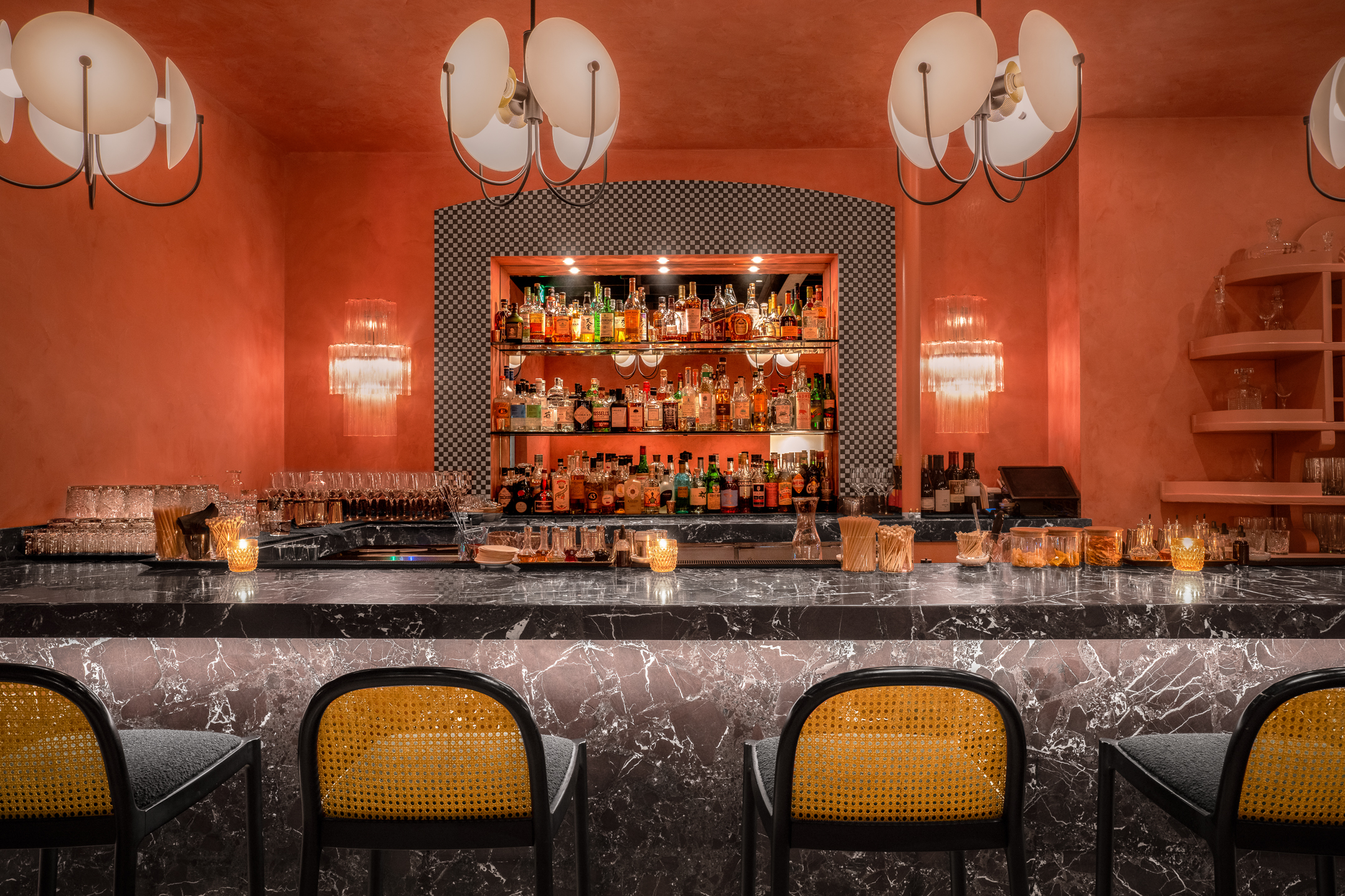 A bar with a marble countertop, barstools, and shelves with bottles