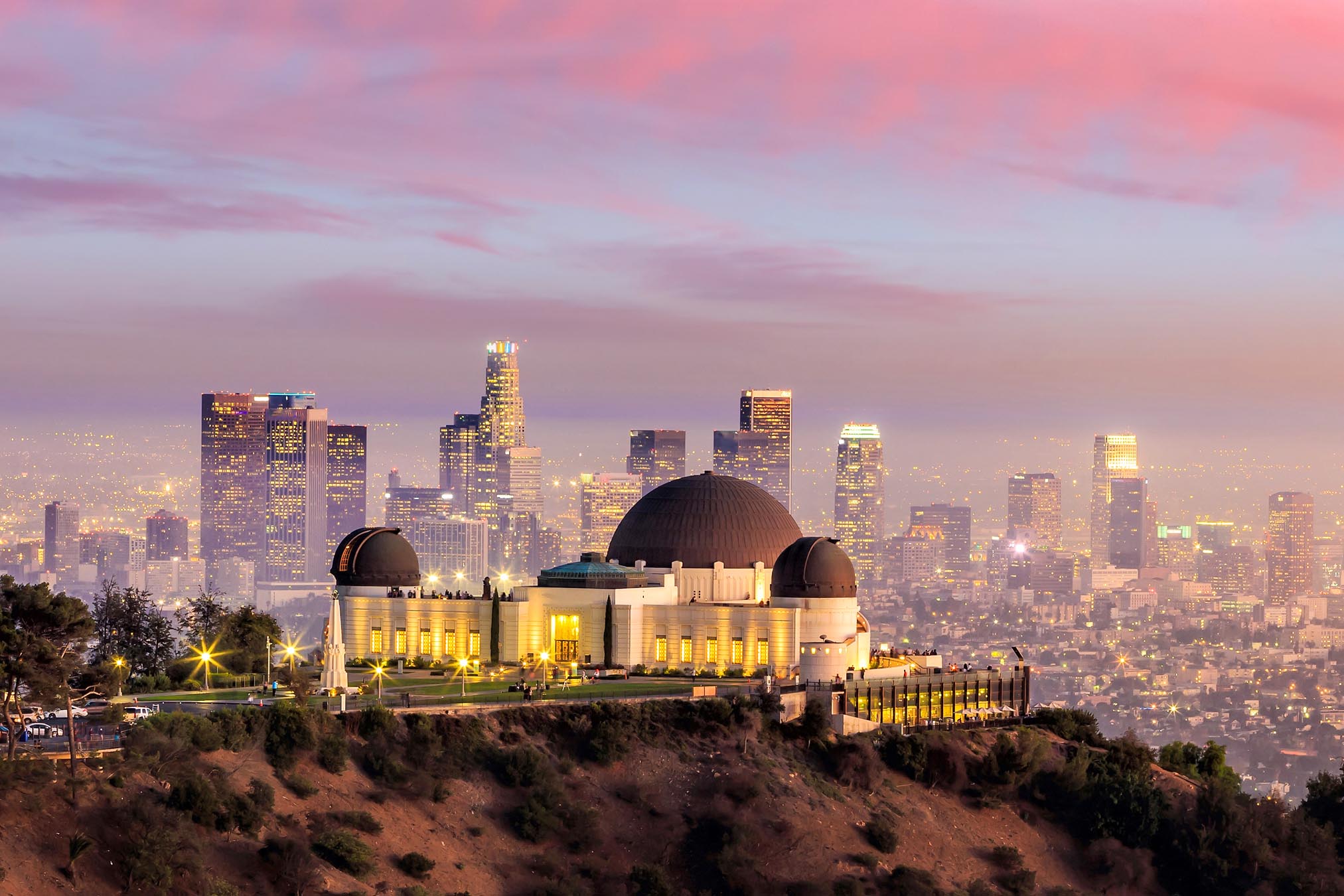 A city skyline at sunset with a large observatory in the foreground.